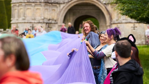 People smiling and laughing at a Cornwall Pride event at Lanhydrock holding a rainbow flag